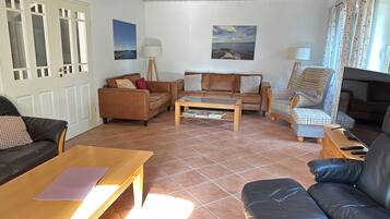 Ein Wohnzimmer mit einem braunen Sofa, einem Holztisch und einem Fernseher auf einem Holzständer.