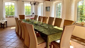 Un comedor con una mesa larga, sillas de mimbre y una araña.