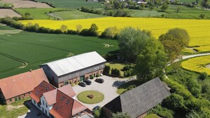 Vista aérea de una granja con campos verdes, un campo amarillo y un edificio de techo rojo con un área de estacionamiento.