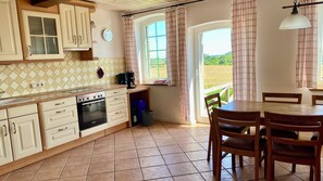 A kitchen with a stove, oven, and cabinets, a dining table with chairs, and a window with curtains. - Vacation Home for 16 People, 8 Bedrooms, 4 Bathrooms, Near Kappeln/Schlei/Baltic Sea, Minimum 2 Nights  (Oersberg)