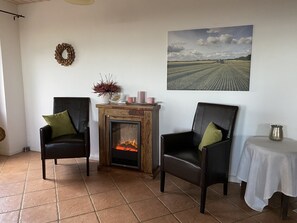 A cozy room with a fireplace, two leather chairs, a small table with a candle, and a landscape painting on the wall. - Vacation Home for 16 People, 8 Bedrooms, 4 Bathrooms, Near Kappeln/Schlei/Baltic Sea, Minimum 2 Nights  (Oersberg)