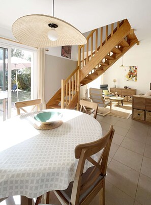 Een eetgedeelte met een ronde tafel, stoelen, een hangende lamp en een houten trap.