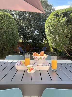A table set outdoors with a table umbrella, two chairs, a bowl of pastries, a mug, and two glasses of orange juice. - Résidence de l’embarcadère - 3-Bedroom House - Gulf of Morbihan (Baden)