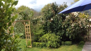 Ein Garten mit einem hölzernen Spalier, verschiedenen Sträuchern und einem blauen Sonnenschirm.