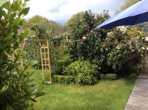 Ein Garten mit einem hölzernen Spalier, verschiedenen Sträuchern und einem blauen Sonnenschirm.