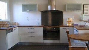 Eine moderne Küche mit weißen Schränken, einer Edelstahl-Dunstabzugshaube, einem eingebauten Backofen und einem Holzespeisesatz mit einem Stuhl.