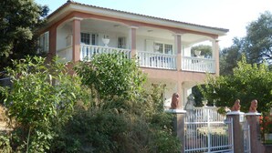 A two-story house with a balcony, surrounded by greenery and a gated entrance. - 100m from downtown and the stores, 300m from the beach and the marina (Porto-Vecchio)