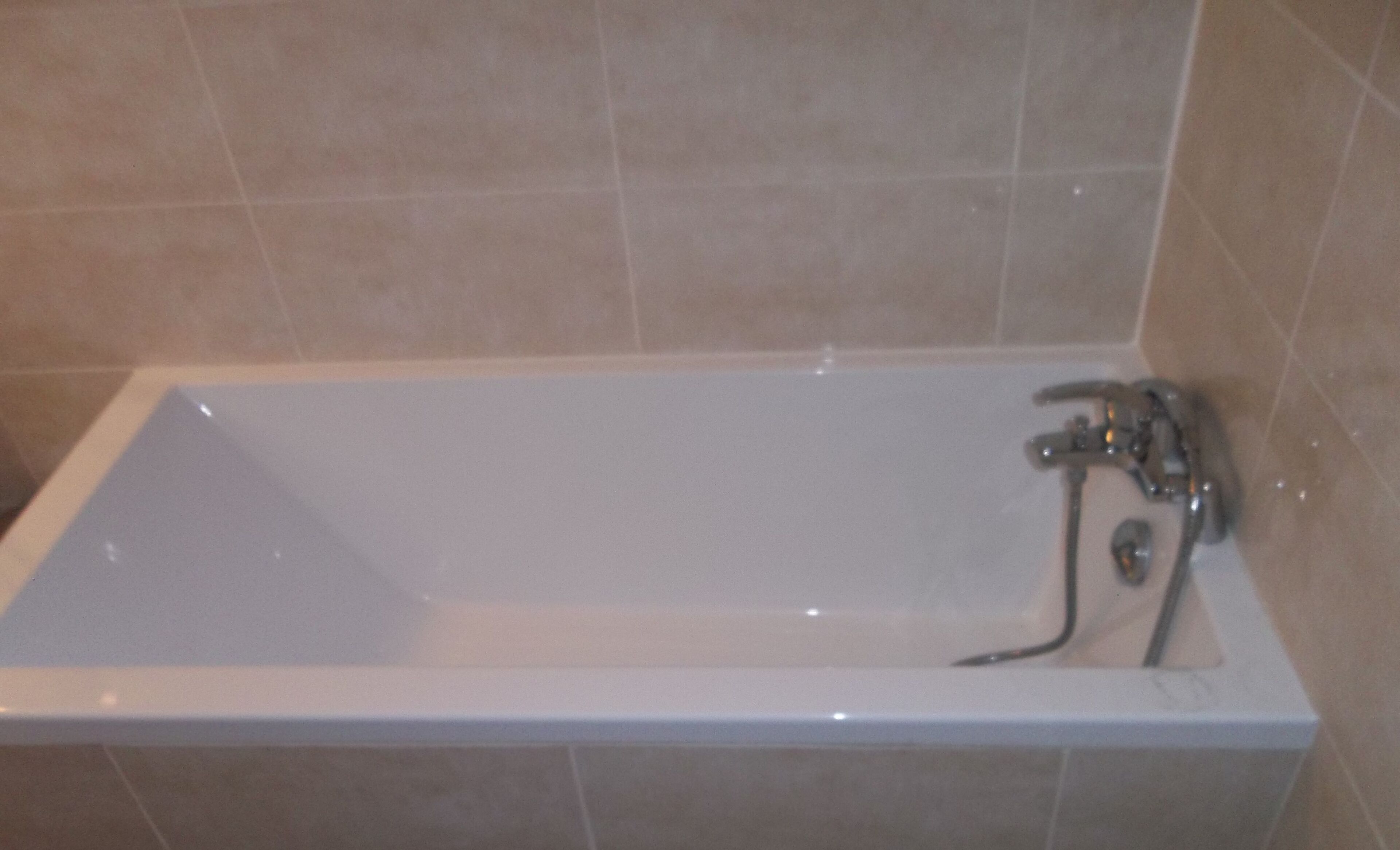 A rectangular bathtub with a single faucet and a handheld showerhead.