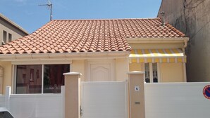 A residential building with a tiled roof, a gated entrance, and a small storefront with a striped awning. - For rent; villa in the center of a resort, quiet area in Valras Beach (Valras-Plage)