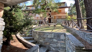 A stone staircase leading to a wooden deck with a stone wall and a building with balconies in the background.