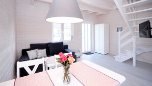 Een moderne woonkamer met een witte trap, een zwarte bank, een eettafel met een bloevas en een grote hanglamp.