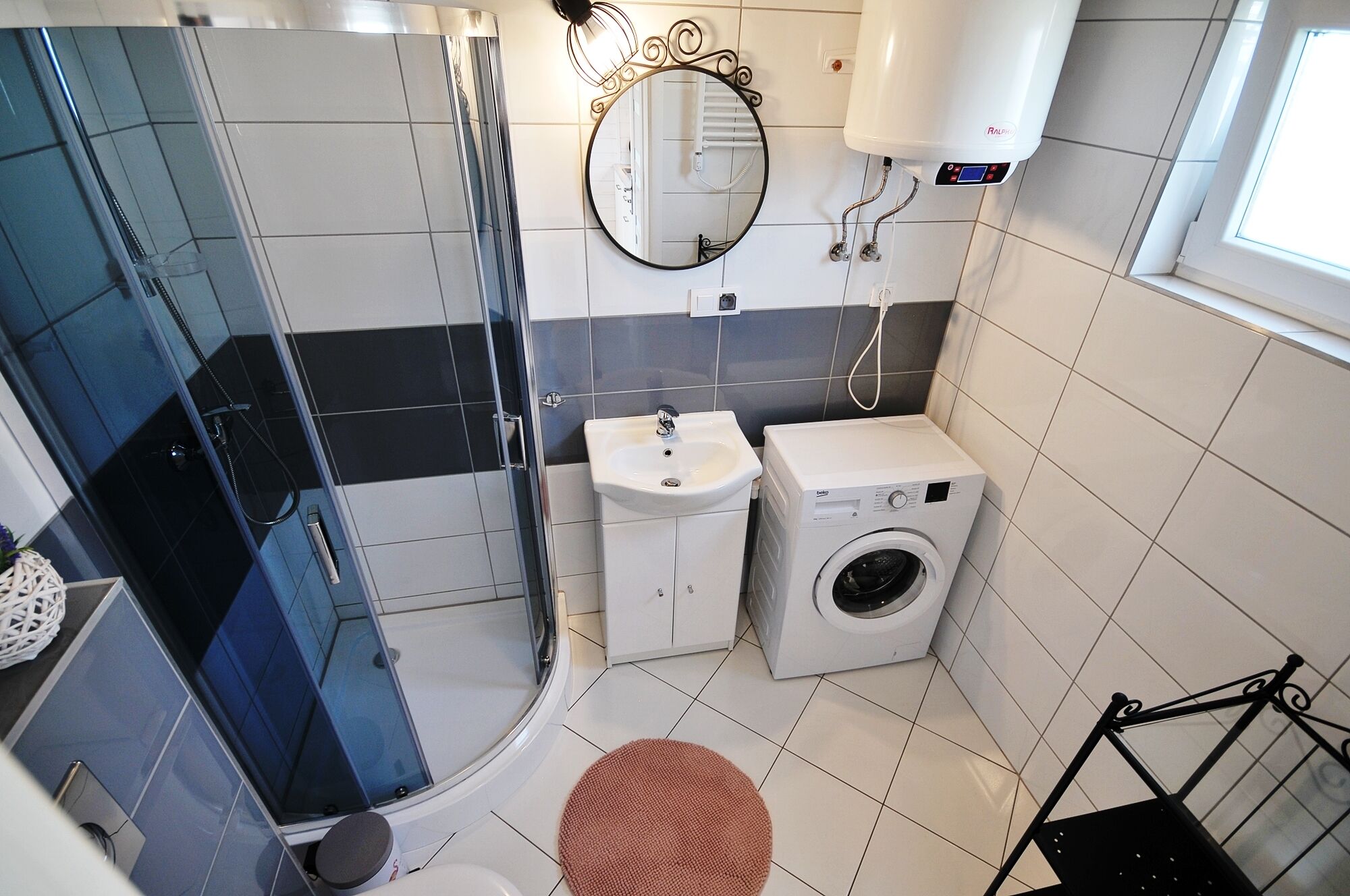 Un bagno moderno con box doccia in vetro, lavabo, lavatrice e specchio.