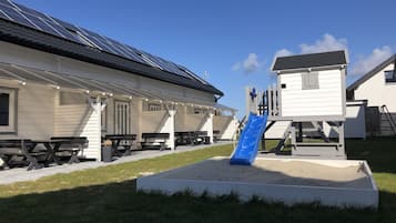 Un parque infantil con un tobogán azul y mesas de picnic en un espacio cubierto de césped.