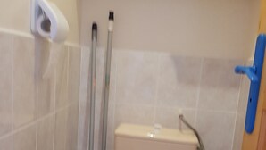 Un baño con inodoro, escoba, mopa y un picaporte azul.