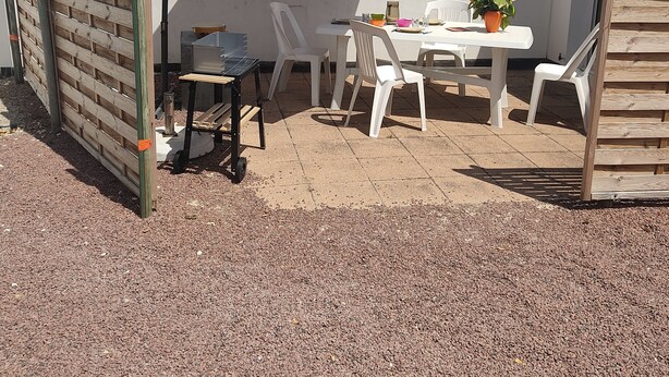 Un patio al aire libre con una mesa, sillas, un paraguas rojo y una cerca de madera.