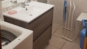 Un baño con lavamanos blanco, espejo y zona de ducha.