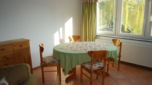 Un comedor con una mesa redonda cubierta con mantel verde, rodeado de sillas de madera con cojines estampados con motivos florales.