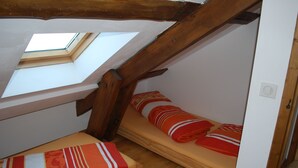 Un dormitorio en ático pequeño con dos camas, vigas de madera, un tragaluz y una puerta blanca.