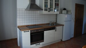 Una cocina compacta con armarios blancos, horno empotrado, lavavajillas y extractor de acero inoxidable.
