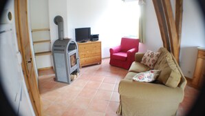 Una sala de estar con chimenea, un sillón rojo, un sofá color crema y un televisor sobre un aparador de madera.