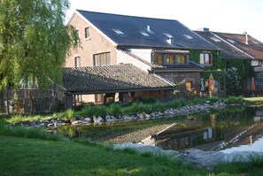 A traditional brick house with a sloped roof, a small pond, and a wooden fence. - Part of an old manor with a large swimming pond at the border triangle B, NL, D (Gemmenich/Plombières)