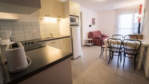 Une cuisine compacte équipée d’un grille-pain, d’un four à micro-ondes et d’un réfrigérateur. Un coin repas avec une table et des chaises est également à disposition.