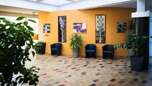 Un vaste espace intérieur doté d’un haut plafond, d’un sol carrelé et de plusieurs chaises disposées le long d’un mur, où sont accrochées des œuvres d’art encadrées.