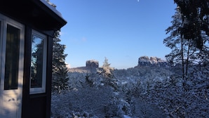 A snow-covered landscape with a view of a mountain range and a house with a window.