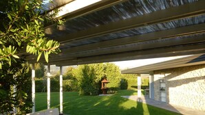 Un patio al aire libre con una zona de estar cubierta, un muro de piedra y un césped cuidado.
