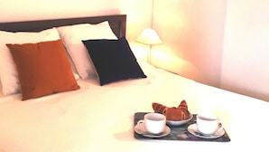 A hotel room with a bed, pillows, a tray with croissants and coffee cups, and a painting of sailboats on the wall. - T2 apartment + 2 terraces + 1 private secure PARKING + WIFI + TV. (Biarritz)
