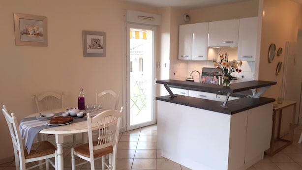A kitchen with white cabinets, a dining table with chairs, and a small island with a black countertop. - T2 apartment + 2 terraces + 1 private secure PARKING + WIFI + TV. (Biarritz)
