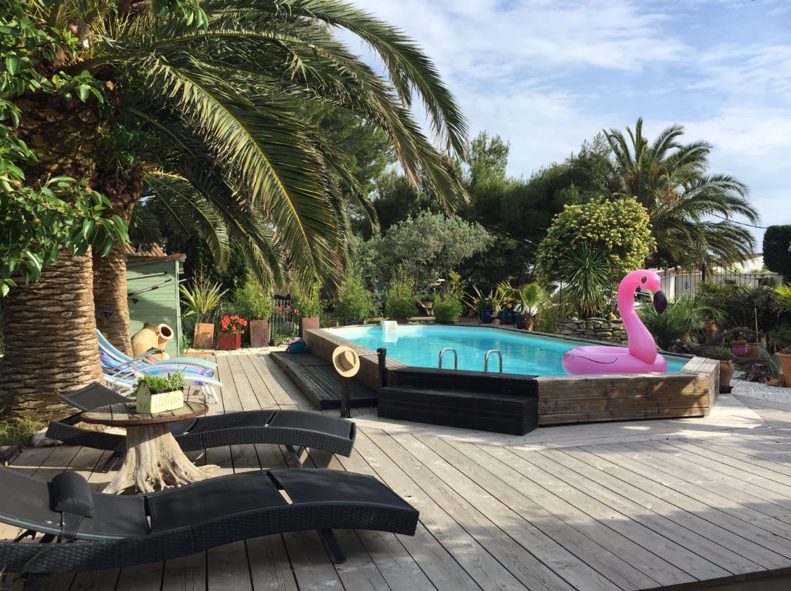 Une terrasse en bois avec une piscine, des chaises longues et une statue de flamant rose.