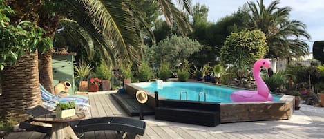 Una terraza de madera con piscina, sillas de descanso y una estatua de flamenco rosa.