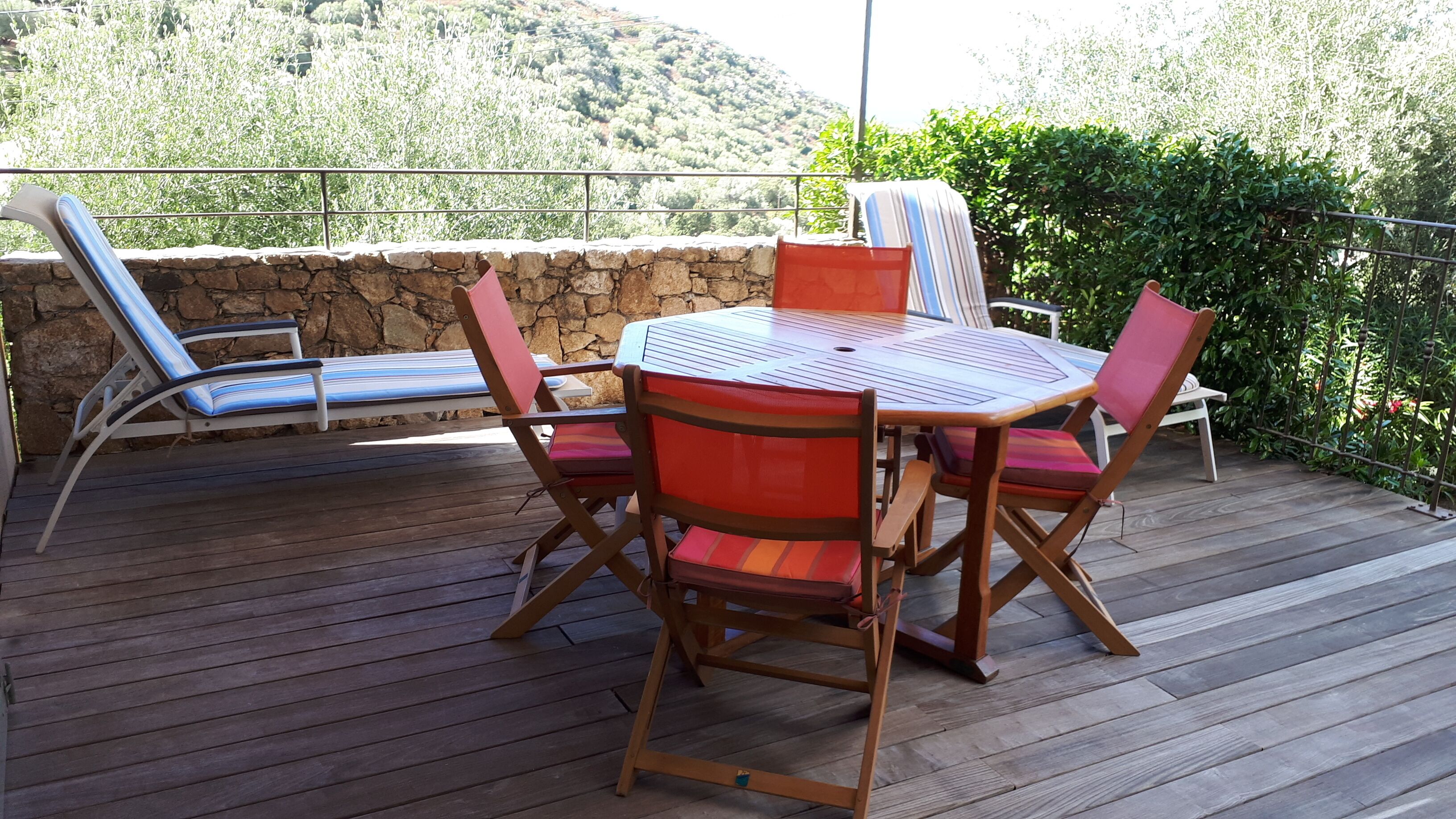 Eine Terrasse im Freien mit einem runden Tisch und vier Stühlen, einer Steinmauer und Blick auf eine hügelige Landschaft.