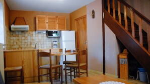 A compact kitchen with wooden cabinets, a microwave, a refrigerator, and a dining table with chairs. - GITE IN THE HEART OF THE GORGES DU TARN (La Malène)