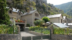 A stone building with a gated entrance, surrounded by lush greenery and a mountainous backdrop. - GITE IN THE HEART OF THE GORGES DU TARN (La Malène)