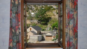 A view through a window with a wooden frame and colorful curtains, revealing a rural landscape with houses and trees. - GITE IN THE HEART OF THE GORGES DU TARN (La Malène)