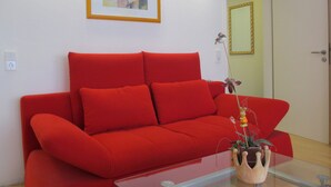A red sofa, a framed picture, and a vase with a plant.