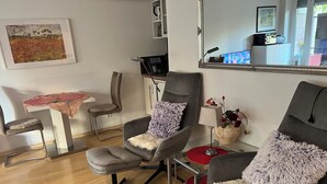 A modern living room with a sofa, armchair, and a small table with a red tablecloth.