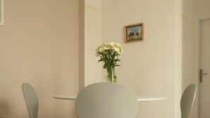 Un comedor con una mesa redonda y dos sillas, un florero con flores, y una puerta al fondo.