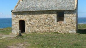 Un edificio de piedra con techo inclinado, una chimenea y una ventana pequeña.