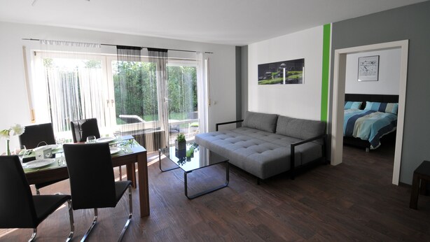 A modern living room with a sofa, dining table, chairs, and a glass coffee table.