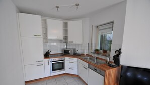 A modern kitchen with white cabinets, a microwave, an oven, a sink, and a television.