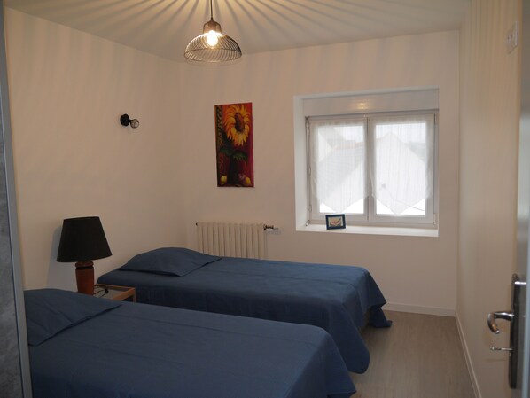 A room with two beds, a window with curtains, a radiator, a wall-mounted lamp, and a painting. - House on enclosed land of 1100 m2, 200 m from the beach Correjou dog accepted (Plouguerneau)