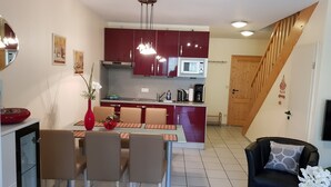 Een moderne keuken met rode kastjes, een eethoek met een tafel en stoelen, en een trap naar een bovenverdieping.