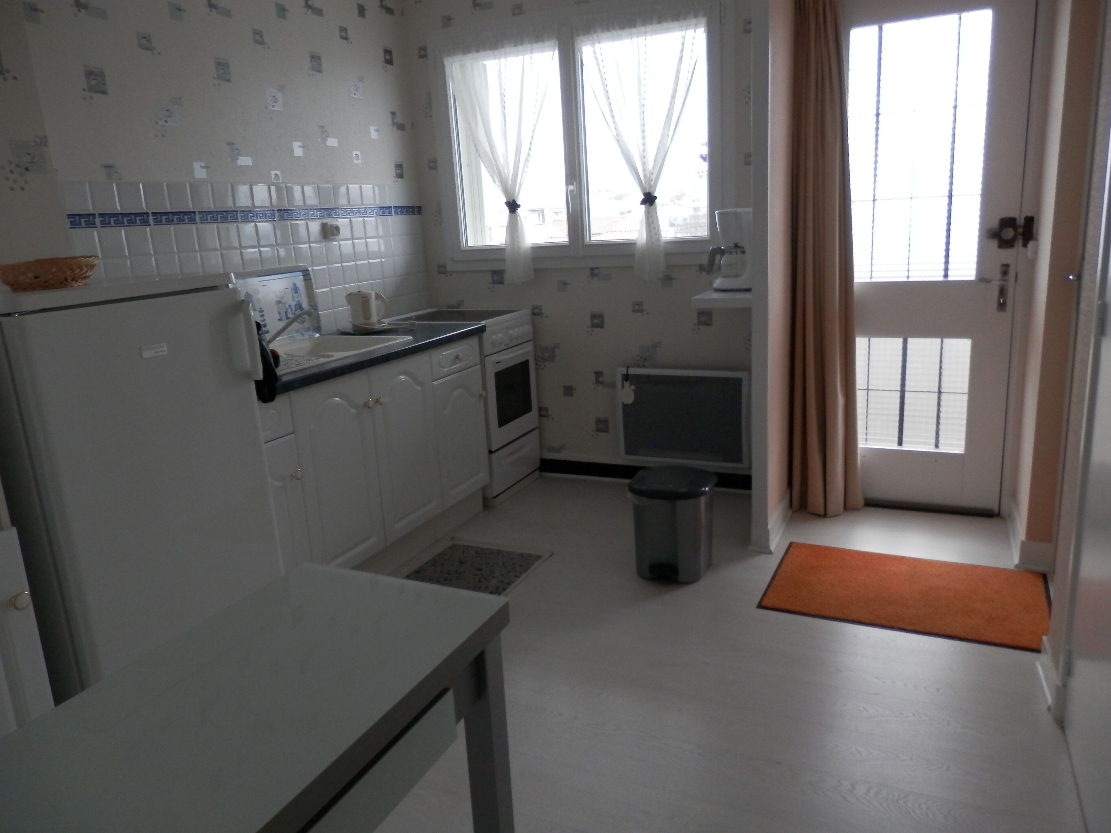 A compact kitchen with white cabinets, a sink, a stove, and a trash bin. - Apartment in very quiet building (Royan)