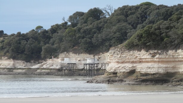 A beach with a rocky cliff and a wooden structure with tables and chairs. - Apartment in very quiet building (Royan)