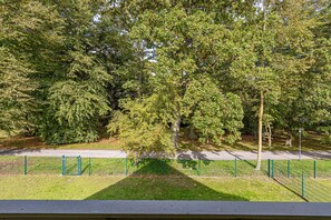 En park med en asfalterad gångväg, grönt staket och träd.
