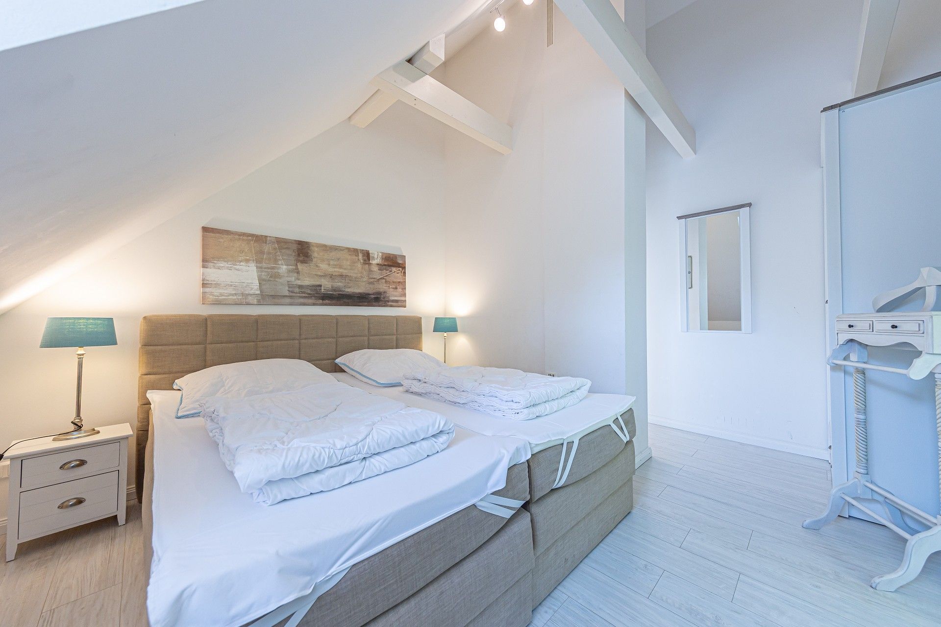 A bedroom with a large bed, two bedside tables, a wall-mounted painting, and a mirror.