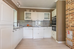 Cocina con armarios blancos, encimera de madera y pared de ladrillo.